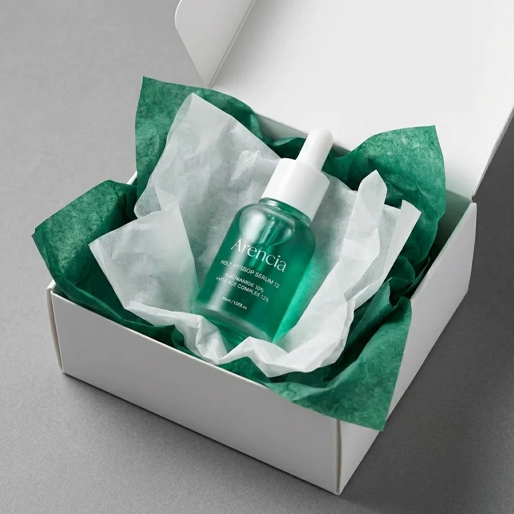 Angle : Vue oblique à mi-hauteur.  Scène : Le flacon d'Arencia est présenté à l'intérieur d'un coffret de livraison premium en carton blanc mat ouvert. Le produit est niché au milieu d'une superposition de papiers de soie froissés de deux couleurs : l'un blanc laiteux, l'autre vert émeraude pour rappeler le flacon.  Fond & Lumière : Surface de studio mate et contemporaine grise. Éclairage uniforme et très lumineux, mettant en valeur l'aspect e-commerce haut de gamme. (gemini-3.1-flash-image-preview)