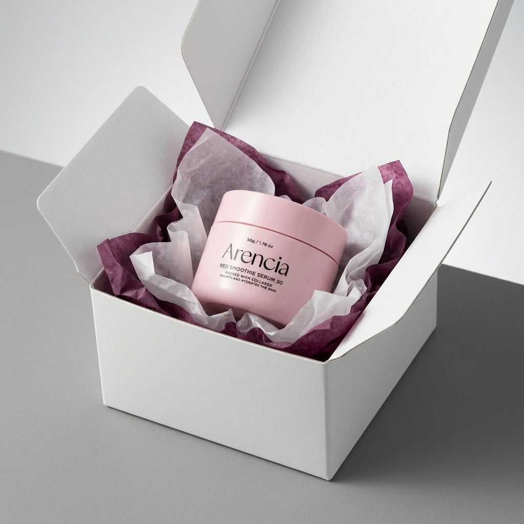 Angle : Vue oblique à mi-hauteur.  Scène : Le pot d'Arencia est fermé avec son couvercle. Il est présenté à l'intérieur d'un coffret de livraison premium en carton blanc mat ouvert. Le produit est niché au milieu d'une superposition de papiers de soie froissés de deux couleurs : l'un blanc laiteux, l'autre rouge pourpre profond pour rappeler la couleur intense du sérum.  Fond & Lumière : Surface de studio mate et contemporaine grise. Éclairage uniforme et très lumineux, mettant en valeur l'aspect e-commerce