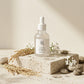 Angle : 45° héro  Le flacon Beauty of Joseon Glow Deep Serum – Rice + Alpha-Arbutin posé sur un socle en travertin clair, entouré d'épis de riz, de fleurs blanches, de gouttes d'eau et de pierres naturelles. Fond crème minimaliste, lumière naturelle du matin, ombres douces, photographie publicitaire ultra réaliste, qualité studio, haute définition. (gemini-3.1-flash-image-preview)