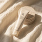 L'Angle : Vue de dessus (flat-lay) structurée et moderne.  Le Fond : Un drap ou une serviette en lin lavé couleur crème, légèrement plissé pour donner du relief.  Le Prompt :  Architectural flat-lay photography of a beige skincare tube placed diagonally on a softly wrinkled cream-colored linen fabric. Beside the tube, a neat stack of neutral-toned stone coasters. Striking but soft morning light creating long, elegant shadows across the fabric. High-fashion cosmetic catalog look, minimal, clean, and calming 