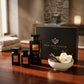 Un plan large à 45 degrés du coffret et des trois flacons de image_221fc1.jpg exposés sur une table en bois d'acajou précieux et poli. À côté des bouteilles, une coupelle en céramique artisanale contient des bâtons de vanille de Madagascar et des tranches de poire fraîche. Une lumière douce et rasante traverse la pièce, installant une atmosphère chaleureuse de spa privé et de soin quotidien de luxe. Style : Campagne éditoriale luxueuse. (gemini-3.1-flash-image-preview)
