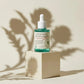 Angle : Centré, pile de face (Eye-level).  Scène : Le flacon de l'image image_cd8746.jpg se tient seul sur un bloc cubique minimaliste laqué crème mat. L'intérêt de l'image repose entièrement sur la mise en scène de la lumière.  Fond & Lumière : Fond monochrome blanc cassé. Une lumière dure traverse des feuilles d'artichaut et des feuillages hors champ, projetant une ombre chinoise floue, poétique et parfaitement découpée sur le mur et sur le flacon. (gemini-3-pro-image-preview)