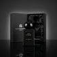 Angle : Vue de face, composition centrée et majestueuse.  Fond : Un fond studio abstrait et minimaliste gris anthracite mat.  Le Prompt à copier :  Photographie publicitaire de parfum de prestige. Un luxueux coffret cadeau noir "Gris Montaigne Paris" est élégamment ouvert au second plan, révélant son intérieur satiné. Juste devant, au premier plan, le flacon de parfum noir mat "OUD KAMARE" et son bouchon globe brillant trônent sur un sol en miroir noir hautement réfléchissant. La lumière du studio crée un h