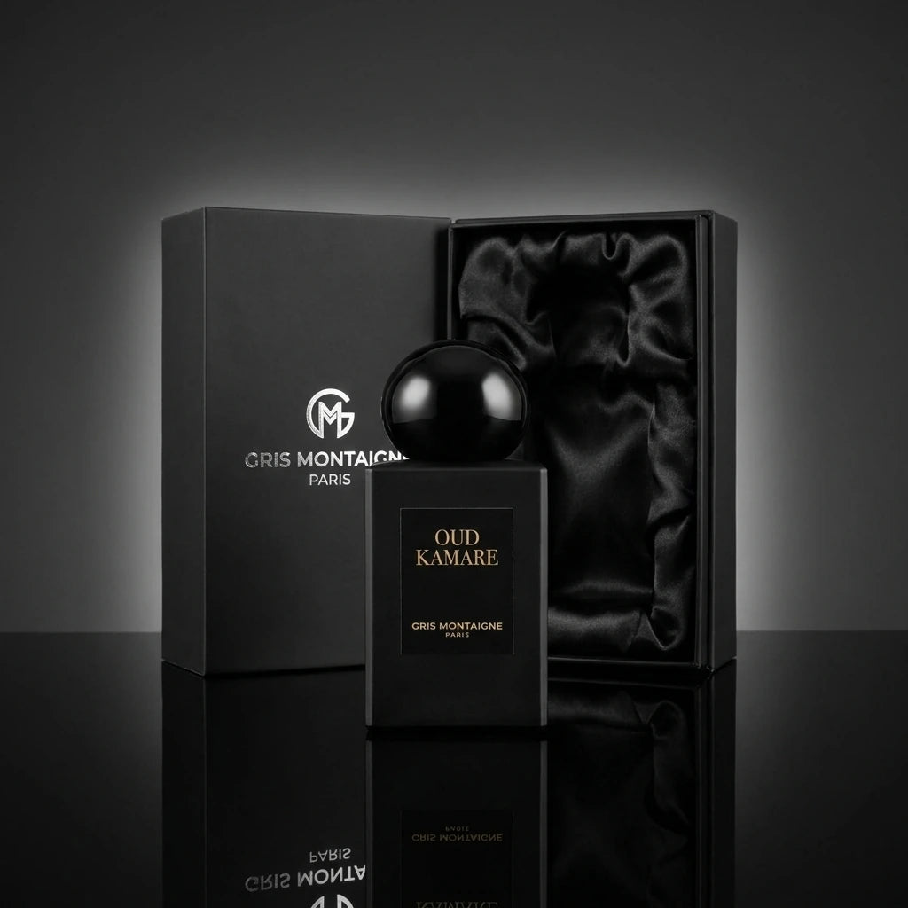 Angle : Vue de face, composition centrée et majestueuse.  Fond : Un fond studio abstrait et minimaliste gris anthracite mat.  Le Prompt à copier :  Photographie publicitaire de parfum de prestige. Un luxueux coffret cadeau noir "Gris Montaigne Paris" est élégamment ouvert au second plan, révélant son intérieur satiné. Juste devant, au premier plan, le flacon de parfum noir mat "OUD KAMARE" et son bouchon globe brillant trônent sur un sol en miroir noir hautement réfléchissant. La lumière du studio crée un h
