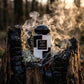 L'idée : Ancrer le parfum dans la terre et le bois brûlé pour exprimer la puissance du sillage.  Le Prompt à copier :  Photographie de produit brute et texturée en contre-plongée. Le flacon "BLACK & WHITE" trône au cœur d'une souche d'arbre centenaire calcinée, révélant le charbon noir et les veines du bois. Des fissures de la souche s'échappe une fine fumée blanche d'encens mystique qui s'enroule autour du flacon. À sa base, de la mousse de chêne argentée et des gousses de vanille sauvage apportent une tou