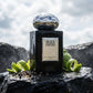 Concept de shooting : Un décor islandais brut où la roche volcanique rencontre la fraîcheur de l'eau pure.  Le Prompt à copier :  Une photographie de shooting e-commerce haut de gamme en extérieur. Au centre, le flacon de parfum noir laqué brillant "BLACK EMPIRE" avec son bouchon chromé effet miroir argenté. Le flacon est posé de manière stable sur un rocher de basalte noir brut, texturé et ruisselant d'eau. Autour de sa base, des écorces de bergamote fraîchement pressées et des baies de poivre noir concass