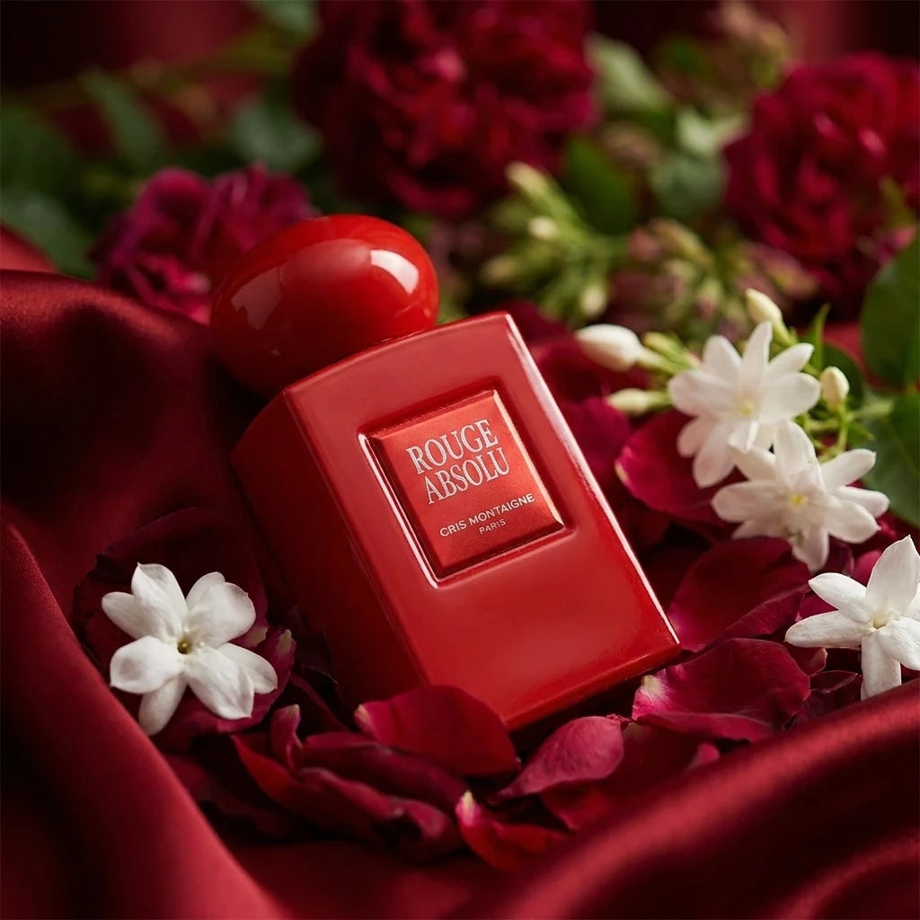 Concept de shooting : Une composition feutrée et théâtrale qui met en avant la volupté des fleurs de caractère.  Le Prompt à copier :  Une photographie de produit style nature morte organique et poétique. Le flacon rectangulaire rouge laqué brillant "ROUGE ABSOLU" est installé au creux d'un drapé fluide en soie rouge opulente. Le flacon émerge subtilement d'un lit dense de pétales de roses de Damas rouge sombre et de fleurs de jasmin blanc royal écloses. Une lumière diffuse et tamisée de style clair-obscur 