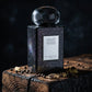 Un plan moyen et rigoureusement frontal du flacon de parfum image_5.png posé au centre d’un bloc de bois de cèdre calciné et texturé. À l’arrière-plan, un éclairage subtil crée un jeu de reflets sur la texture pailletée noire du corps de image_5.png, rappelant une galaxie étoilée. Quelques cristaux de poivre noir et des gousses de cardamome éclatées entourent la base. Style : Photographie publicitaire de luxe, atmosphère mystérieuse et sombre. (gemini-3-pro-image-preview)