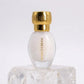 Un plan moyen frontal du petit flacon ovoïde de image_2f6169.jpg isolé, posé sur un bloc de quartz cristallin transparent. Une lumière douce traverse la scène par l'avant, révélant la texture blanche et laiteuse du jus à travers le verre transparent et faisant briller l'inscription verticale jaune-dorée 'MANGO CREAM' de image_2f6169.jpg. Le bouchon doré cannelé capte un éclat lumineux linéaire parfait. Style : Photographie de produit haut de gamme et épurée. (gemini-3-pro-image-preview)
