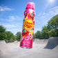 Low-angle shot (contre-plongée) of a 150ml Chupa Chups "Strawberry Swirl" Body Spray bottle frozen mid-air, spinning slightly. The bottle is captured just above a clean concrete outdoor skatepark under a bright blue summer sky. High shutter speed photography, realistic motion blur on the background, bright natural sunlight creating a sharp reflection on the aluminum bottle. Professional lifestyle ad, commercial look, photorealistic, depth of field, vivid realistic colors, no fantasy elements. (gpt-image-1.5